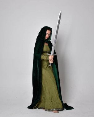 Fantezi kadife pelerinli yeşil ortaçağ elbisesi giyen kızıl saçlı kızın tam boy portresi. Stüdyonun arka planında yalnız poz vermek.