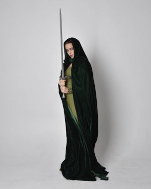 Fantezi kadife pelerinli yeşil ortaçağ elbisesi giyen kızıl saçlı kızın tam boy portresi. Stüdyonun arka planında yalnız poz vermek.