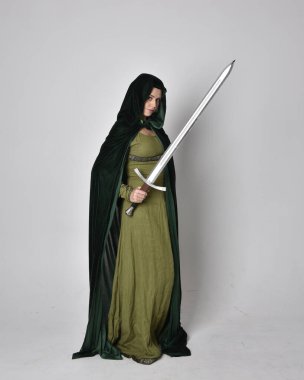 Fantezi kadife pelerinli yeşil ortaçağ elbisesi giyen kızıl saçlı kızın tam boy portresi. Stüdyonun arka planında yalnız poz vermek.