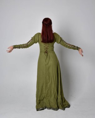 Yeşil ortaçağ elbisesi giyen kızıl saçlı kızın tam boy portresi. Stüdyonun arka planında yalnız poz vermek.