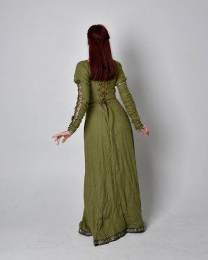 Yeşil ortaçağ elbisesi giyen kızıl saçlı kızın tam boy portresi. Stüdyonun arka planında yalnız poz vermek.