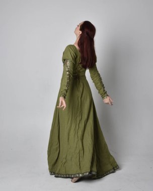 Yeşil ortaçağ elbisesi giyen kızıl saçlı kızın tam boy portresi. Stüdyonun arka planında yalnız poz vermek.