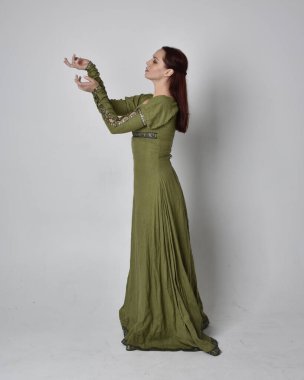 Yeşil ortaçağ elbisesi giyen kızıl saçlı kızın tam boy portresi. Stüdyonun arka planında yalnız poz vermek.