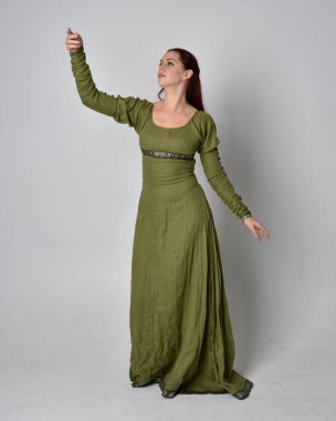 Yeşil ortaçağ elbisesi giyen kızıl saçlı kızın tam boy portresi. Stüdyonun arka planında yalnız poz vermek.