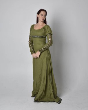 Yeşil ortaçağ elbisesi giyen kızıl saçlı kızın tam boy portresi. Stüdyonun arka planında yalnız poz vermek.