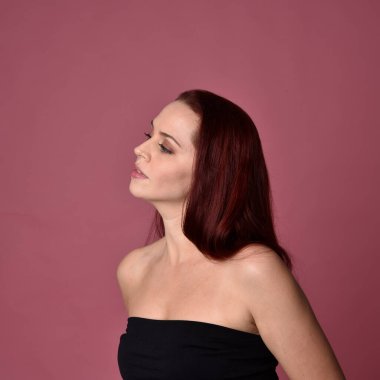 Pembe stüdyo arka planında anlamlı yüz hatları olan kızıl saçlı bir kadının portresi..