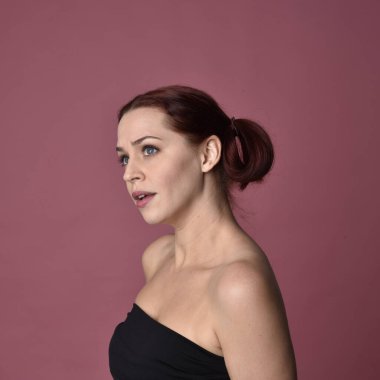 Pembe stüdyo arka planında anlamlı yüz hatları olan kızıl saçlı bir kadının portresi..