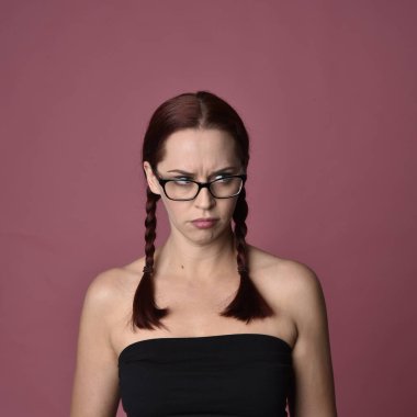 Pembe stüdyo arka planında ifade edici yüz hatları ve gözlüğü olan kızıl saçlı bir kadının portresi..