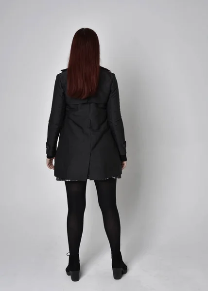 全长肖像一个红头发的女孩穿着黑色外套 格子呢裙和靴子 在摄影棚的背景下 背对着相机站姿 — 图库照片