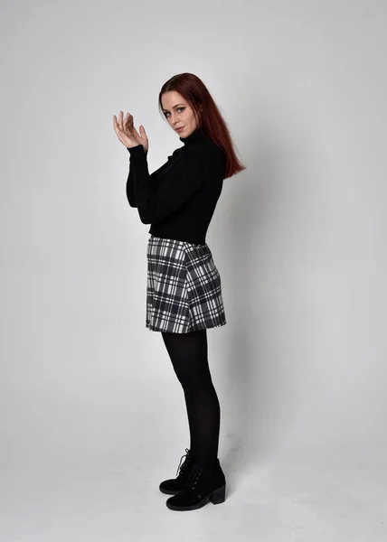 黒のタートルネックセーターを着て 赤い髪の少女の完全な長さの肖像画は スカートとブーツを果たした 撮影所を背景に立ちポーズ — ストック写真