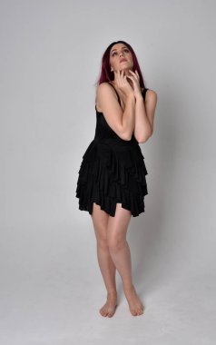 Siyah elbise ve tüylü melek kanatları takan kızıl saçlı bir kızın tam boy portresi. Stüdyo geçmişine karşı poz vermek.