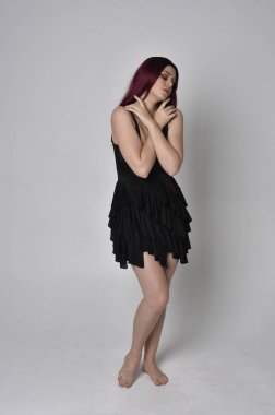 Siyah elbise ve tüylü melek kanatları takan kızıl saçlı bir kızın tam boy portresi. Stüdyo geçmişine karşı poz vermek.