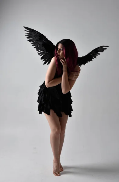 全长肖像一个红头发的女孩穿着黑色衣服和羽毛天使翅膀 在演播室背景下站立姿势 — 图库照片