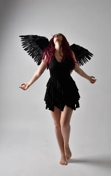 全长肖像一个红头发的女孩穿着黑色衣服和羽毛天使翅膀 在演播室背景下站立姿势 — 图库照片