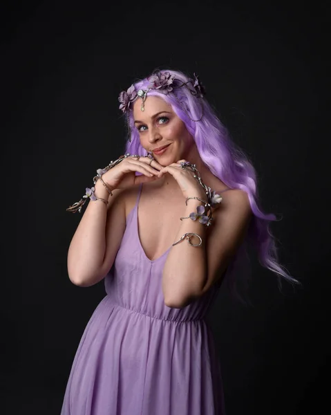 Close up portrait of a purple haired  girl wearing fantasy corset dress with fairy wings and flower crown, casting a spell.  Posing against a dark studio background.