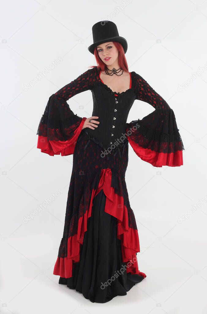full length portrait of red haired woman wearing long black gothic victorian vampire gown. posing on white studio background.