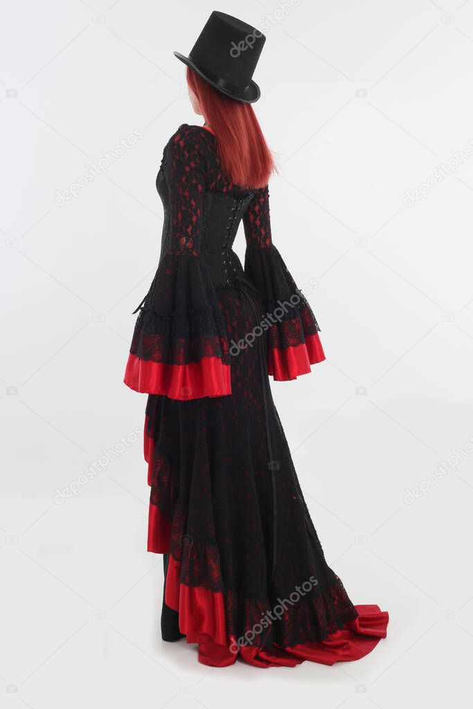 full length portrait of red haired woman wearing long black gothic victorian vampire gown. posing on white studio background.