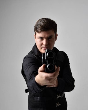 Deri ceket giyen ve elinde bilim kurgu silahı tutan esmer bir adamın portresi. Eylem, gri bir stüdyonun arka planında izole edilmiş.