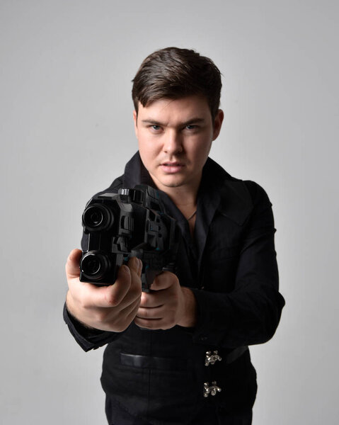 close up portrait of a  brunette man wearing leather jacket  and holding a science fiction gun.  action pose isolated  against a grey studio background.