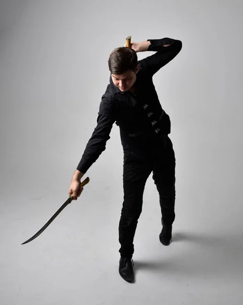 全长肖像一个黑发男人穿着黑色衬衫和哥特式背心拿着剑 在灰色的工作室背景下 站立的动作姿态是孤立的 — 图库照片