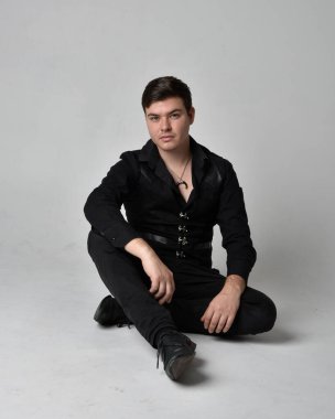 Siyah gömlek ve gotik yelek giyen esmer bir adamın tam boy portresi. Gri bir stüdyonun arka planında izole bir poz..