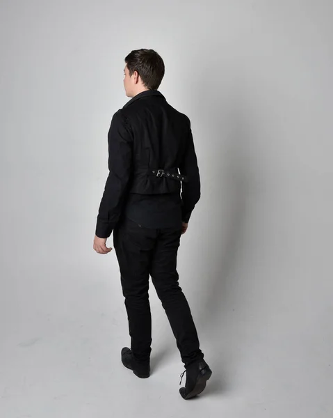 一个黑发男人穿着黑色衬衫和哥特式背心的全长肖像 与灰色工作室背景隔离的站立姿势 — 图库照片