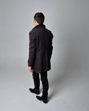 Siyah deri ceket giyen esmer bir adamın tam boy portresi. Geriye dönük poz vermek, kameradan uzaklaşmak gri bir stüdyonun arka planında izole edilmiş..