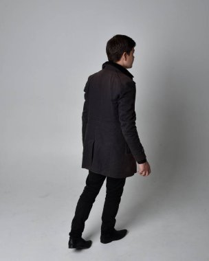 Siyah deri ceket giyen esmer bir adamın tam boy portresi. Geriye dönük poz vermek, kameradan uzaklaşmak gri bir stüdyonun arka planında izole edilmiş..