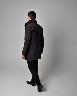 Siyah deri ceket giyen esmer bir adamın tam boy portresi. Geriye dönük poz vermek, kameradan uzaklaşmak gri bir stüdyonun arka planında izole edilmiş..