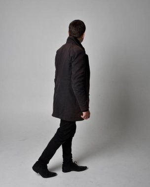 Siyah deri ceket giyen esmer bir adamın tam boy portresi. Geriye dönük poz vermek, kameradan uzaklaşmak gri bir stüdyonun arka planında izole edilmiş..