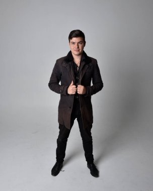 Siyah deri ceket giyen esmer bir adamın tam boy portresi. Gri bir stüdyonun arka planında izole bir şekilde duruyor..