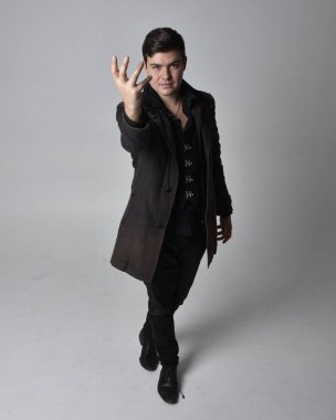 Siyah deri ceket giyen esmer bir adamın tam boy portresi. Gri bir stüdyonun arka planında izole bir şekilde duruyor..