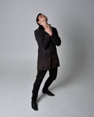 Siyah deri ceket giyen esmer bir adamın tam boy portresi. Gri bir stüdyonun arka planında izole bir şekilde duruyor..