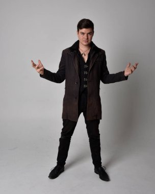 Siyah deri ceket giyen esmer bir adamın tam boy portresi. Gri bir stüdyonun arka planında izole bir şekilde duruyor..