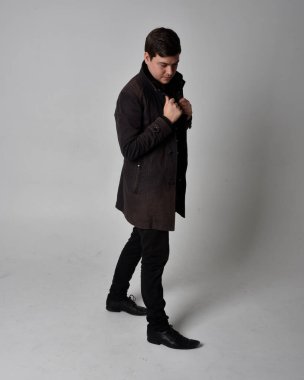 Siyah deri ceket giyen esmer bir adamın tam boy portresi. Gri bir stüdyonun arka planında izole bir şekilde duruyor..