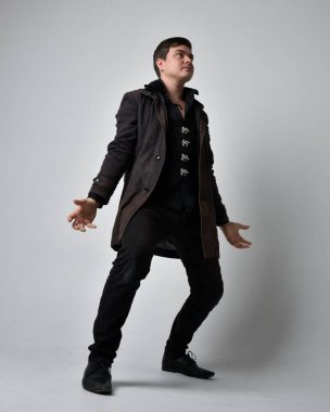 Siyah deri ceket giyen esmer bir adamın tam boy portresi. Gri bir stüdyonun arka planında izole bir şekilde duruyor..