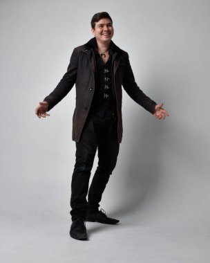 Siyah deri ceket giyen esmer bir adamın tam boy portresi. Gri bir stüdyonun arka planında izole bir şekilde duruyor..