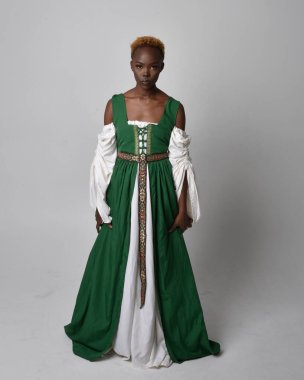 Full length portrait of pretty African woman wearing long green medieval fantasy gown, standing and dancing pose on a light grey studio background. clipart