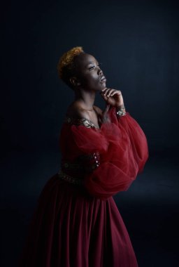 Kırmızı rönesans fantezi elbisesi giyen güzel Afrikalı bir kadının klasik portresi, karanlık bir stüdyo arka planında gölgeli ışıklandırma..