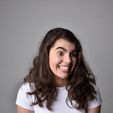 Açık gri stüdyo arka planındaki yüz ifadelerinin üzerinde, doğal kahverengi saçlı genç bir kadının yakın portresi var..