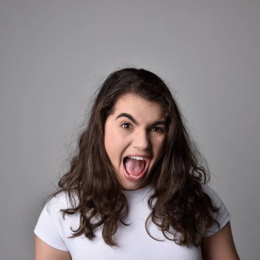 Açık gri stüdyo arka planındaki yüz ifadelerinin üzerinde, doğal kahverengi saçlı genç bir kadının yakın portresi var..