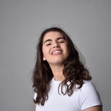 Açık gri stüdyo arka planındaki yüz ifadelerinin üzerinde, doğal kahverengi saçlı genç bir kadının yakın portresi var..