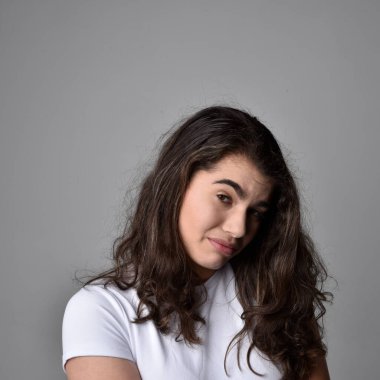 Açık gri stüdyo arka planındaki yüz ifadelerinin üzerinde, doğal kahverengi saçlı genç bir kadının yakın portresi var..