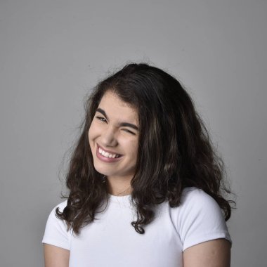 Açık gri stüdyo arka planındaki yüz ifadelerinin üzerinde, doğal kahverengi saçlı genç bir kadının yakın portresi var..