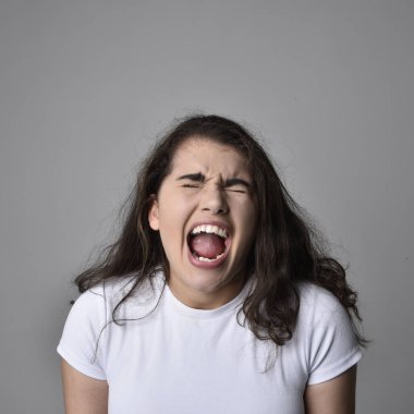 Açık gri stüdyo arka planındaki yüz ifadelerinin üzerinde, doğal kahverengi saçlı genç bir kadının yakın portresi var..