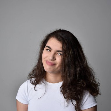 Açık gri stüdyo arka planındaki yüz ifadelerinin üzerinde, doğal kahverengi saçlı genç bir kadının yakın portresi var..