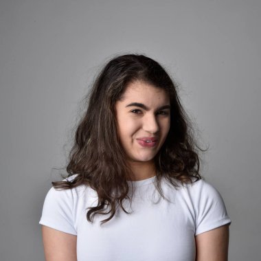 Açık gri stüdyo arka planındaki yüz ifadelerinin üzerinde, doğal kahverengi saçlı genç bir kadının yakın portresi var..