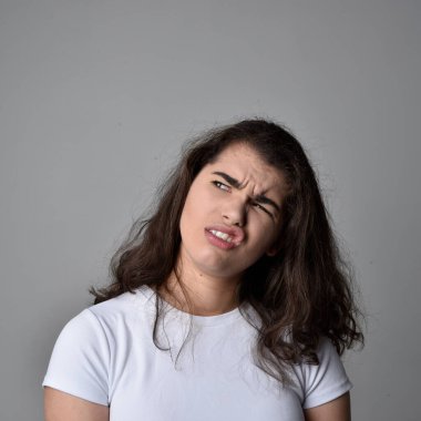 Açık gri stüdyo arka planındaki yüz ifadelerinin üzerinde, doğal kahverengi saçlı genç bir kadının yakın portresi var..