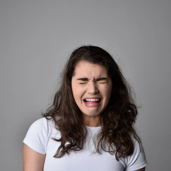 Close up portrait of young woman with natural brown hair, over the top facial expressions on light grey studio background.