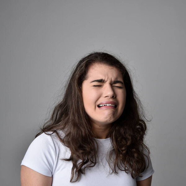 Close up portrait of young woman with natural brown hair, over the top facial expressions on light grey studio background.